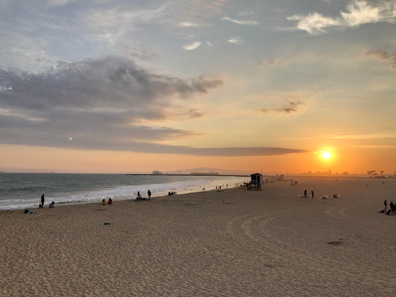 A beach at sunset with people and a lifeguard stand.