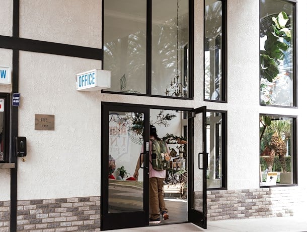 A person entering the office area of a building with a glass door and stucco exterior.