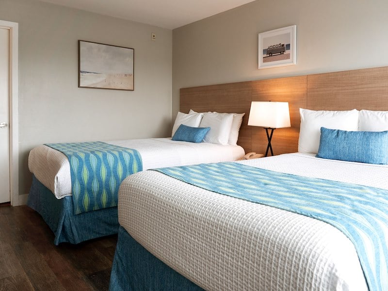 A hotel room with two beds, wooden headboard, and table lamp