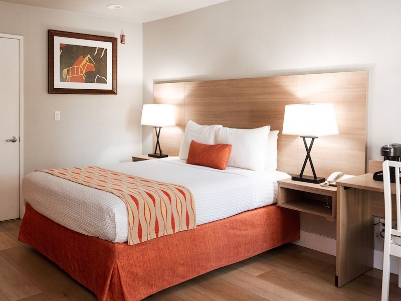 A hotel room with a bed, two lamps, a desk, and a telephone.