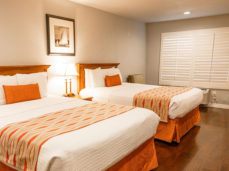 A hotel room with two beds, each with white and orange bedding, a lamp, and a picture frame on the wall.
