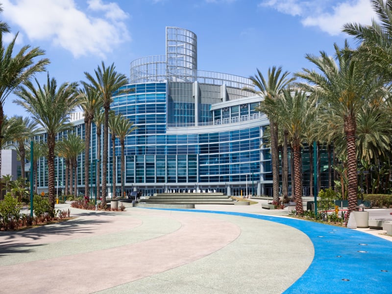 A large, modern building with a curved glass facade and palm trees in front of it.